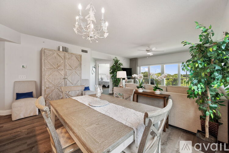 A dining room with a wooden table and chairs, a chandelier, and a large window with a view of the outdoors.