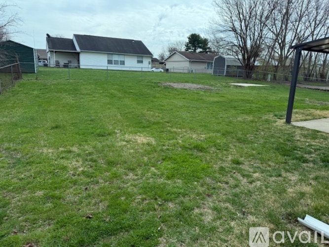 A grassy field with a white house and a fence in the background.