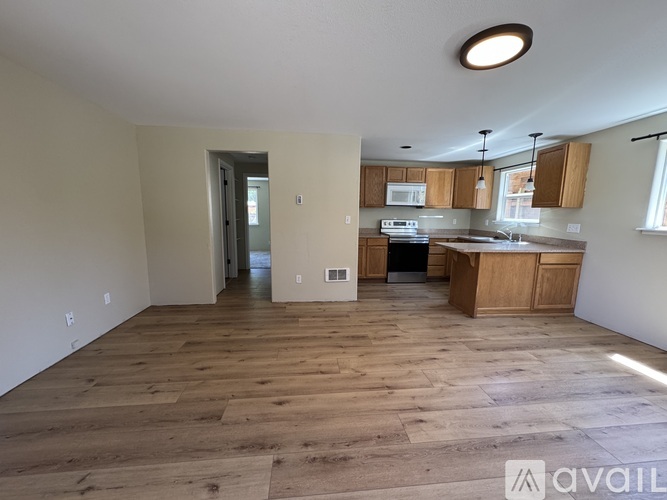 A spacious kitchen and living room with wooden flooring and white walls.