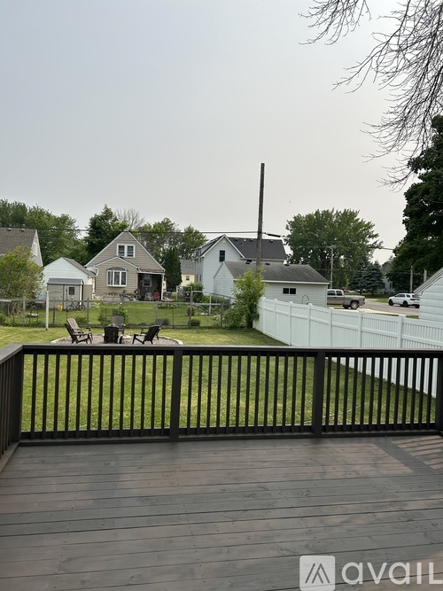 A deck with a railing overlooks a grassy area with houses and trees in the background.