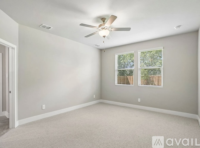 A room with a ceiling fan and two windows.