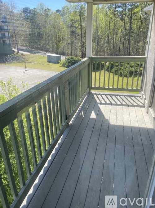 A wooden deck with a railing and a view of a grassy area and trees.