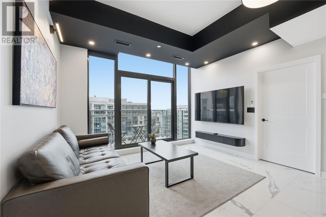 A living room with a grey couch and a large window overlooking a cityscape.