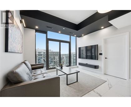 A living room with a grey couch and a large window overlooking a cityscape.