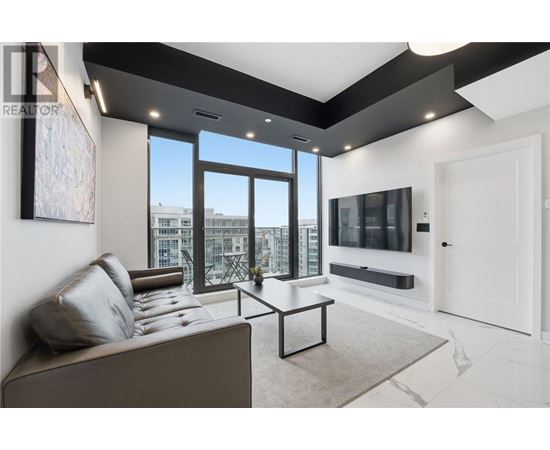 A living room with a grey couch and a large window overlooking a cityscape.