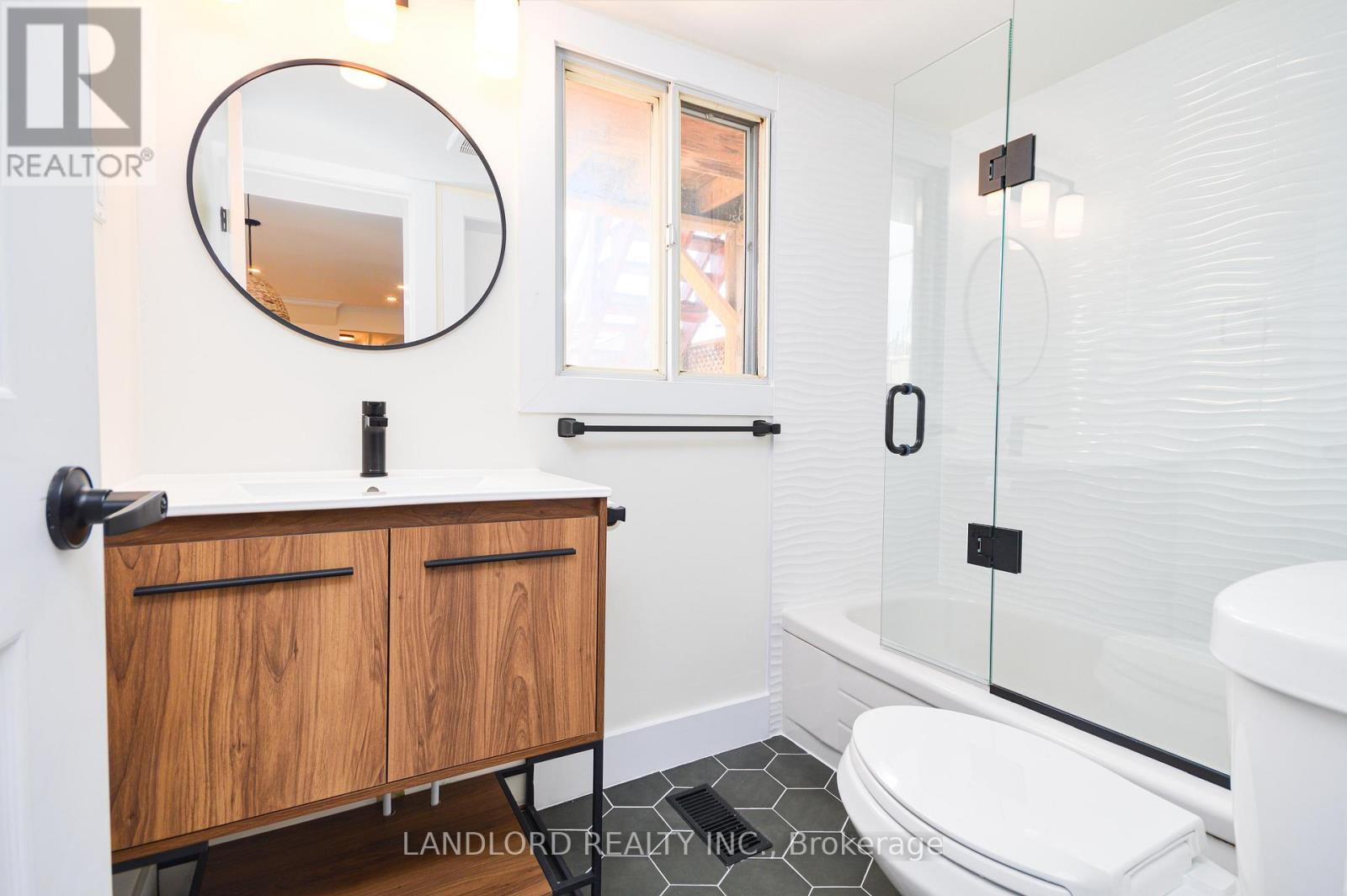 A white bathroom with a wooden cabinet and a glass shower door.