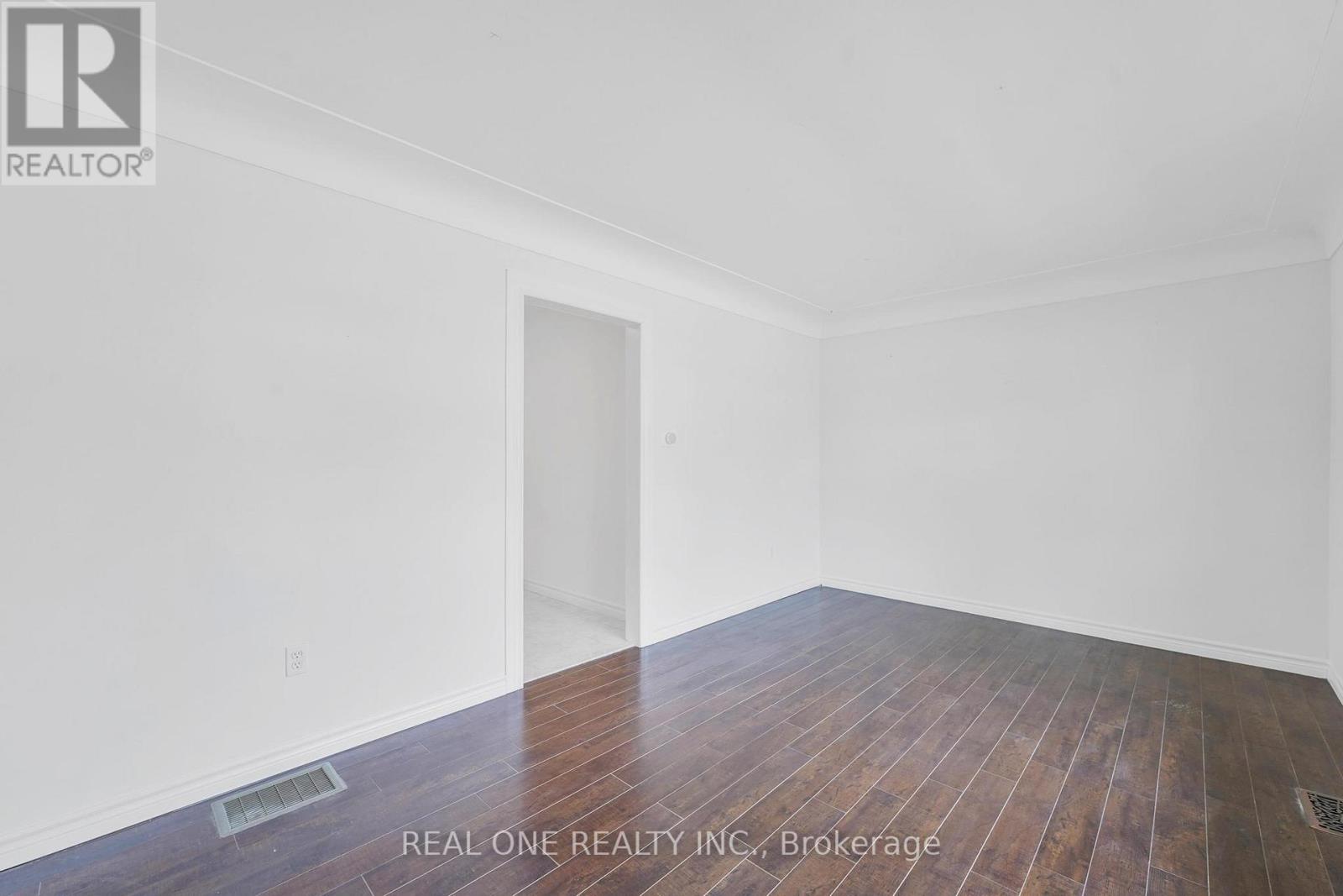 A room with wooden flooring and white walls, with a door and a window.