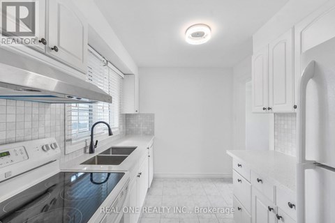 A white kitchen with a stove top oven and a refrigerator.