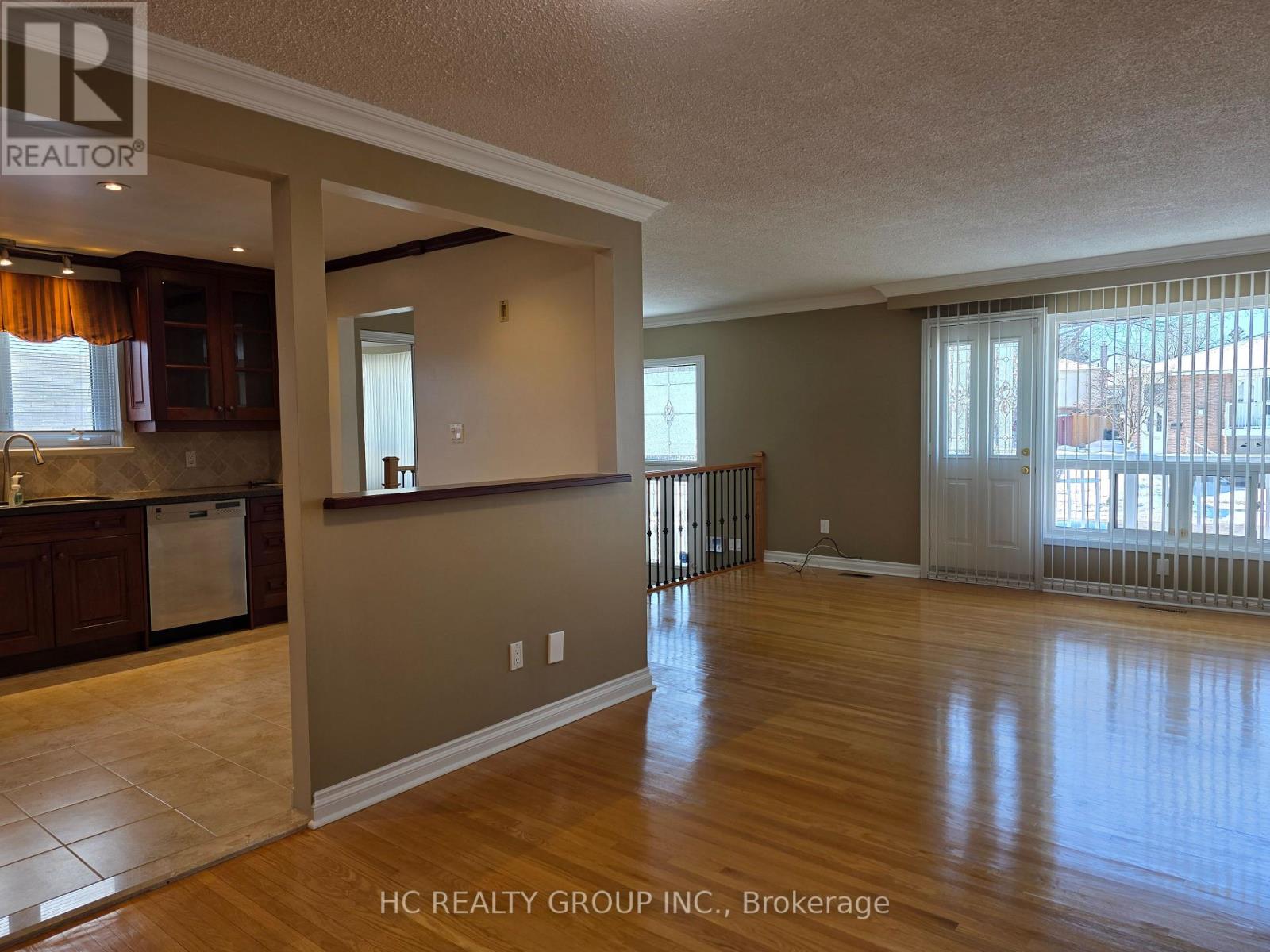 A spacious living room with hardwood floors and a kitchen area to the left.