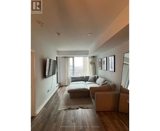 A living room with a grey couch and a flat screen TV mounted on the wall.