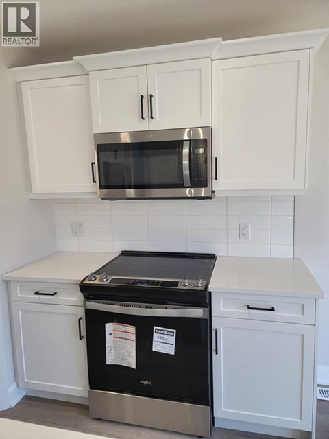 A kitchen with white cabinets and a stainless steel microwave above the stove.