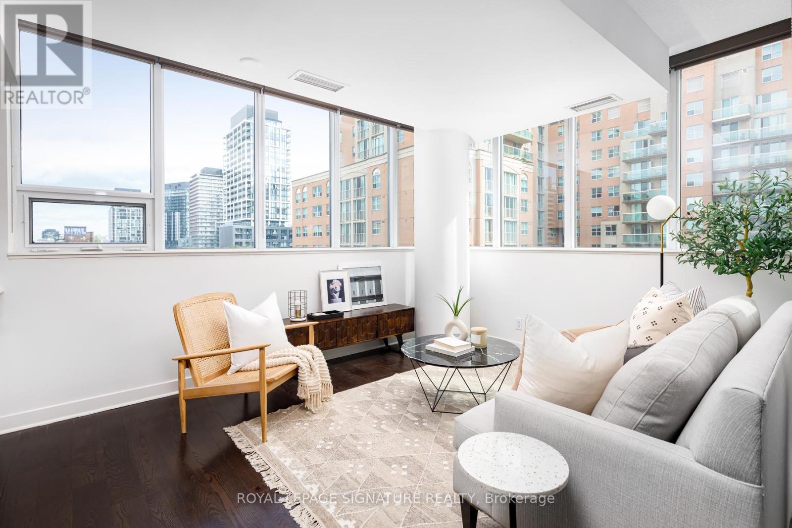 A living room with a grey couch, a wooden chair, a small table, and a large window with a view of the city.