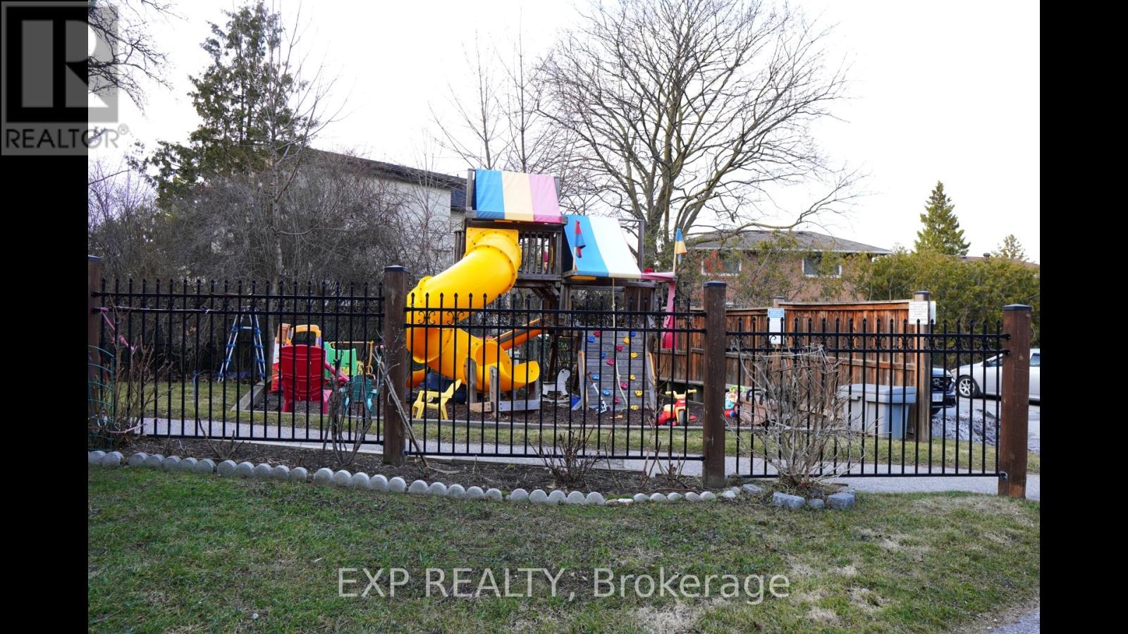 A playground with a yellow slide and a black fence.