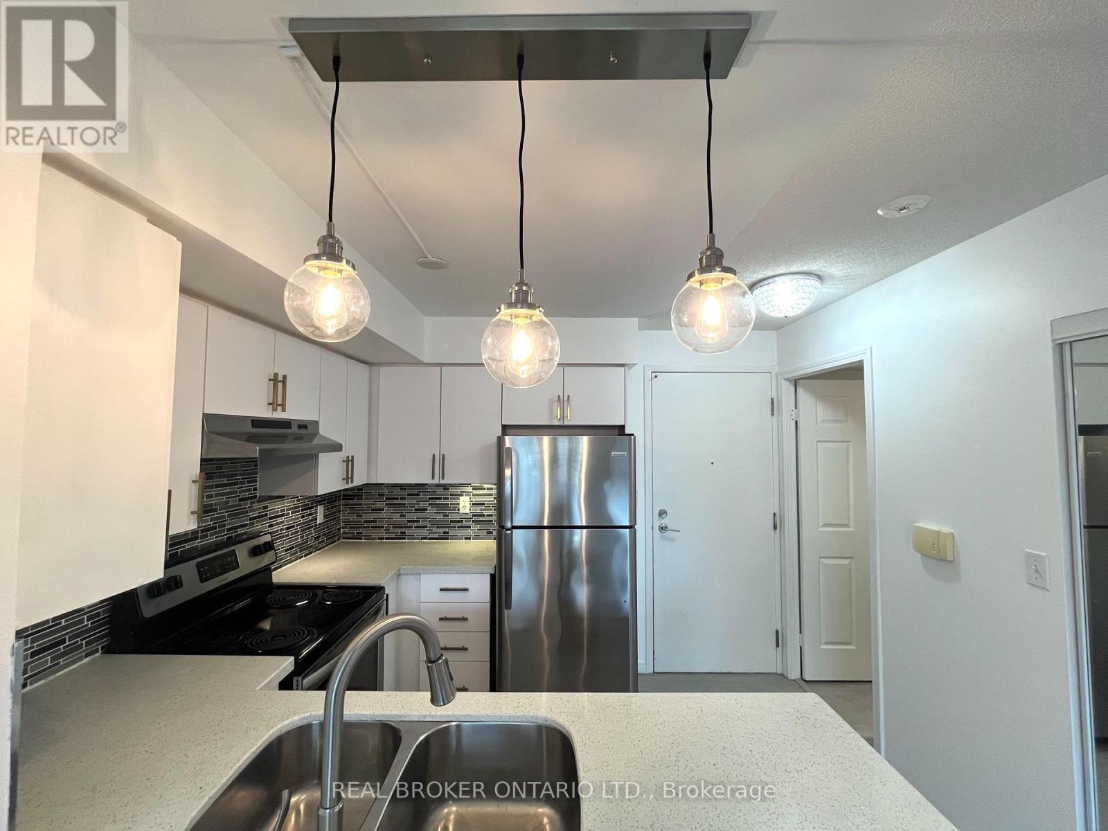 A modern kitchen with a stainless steel refrigerator and pendant lights.