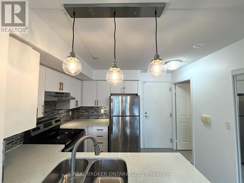 A modern kitchen with a stainless steel refrigerator and pendant lights.