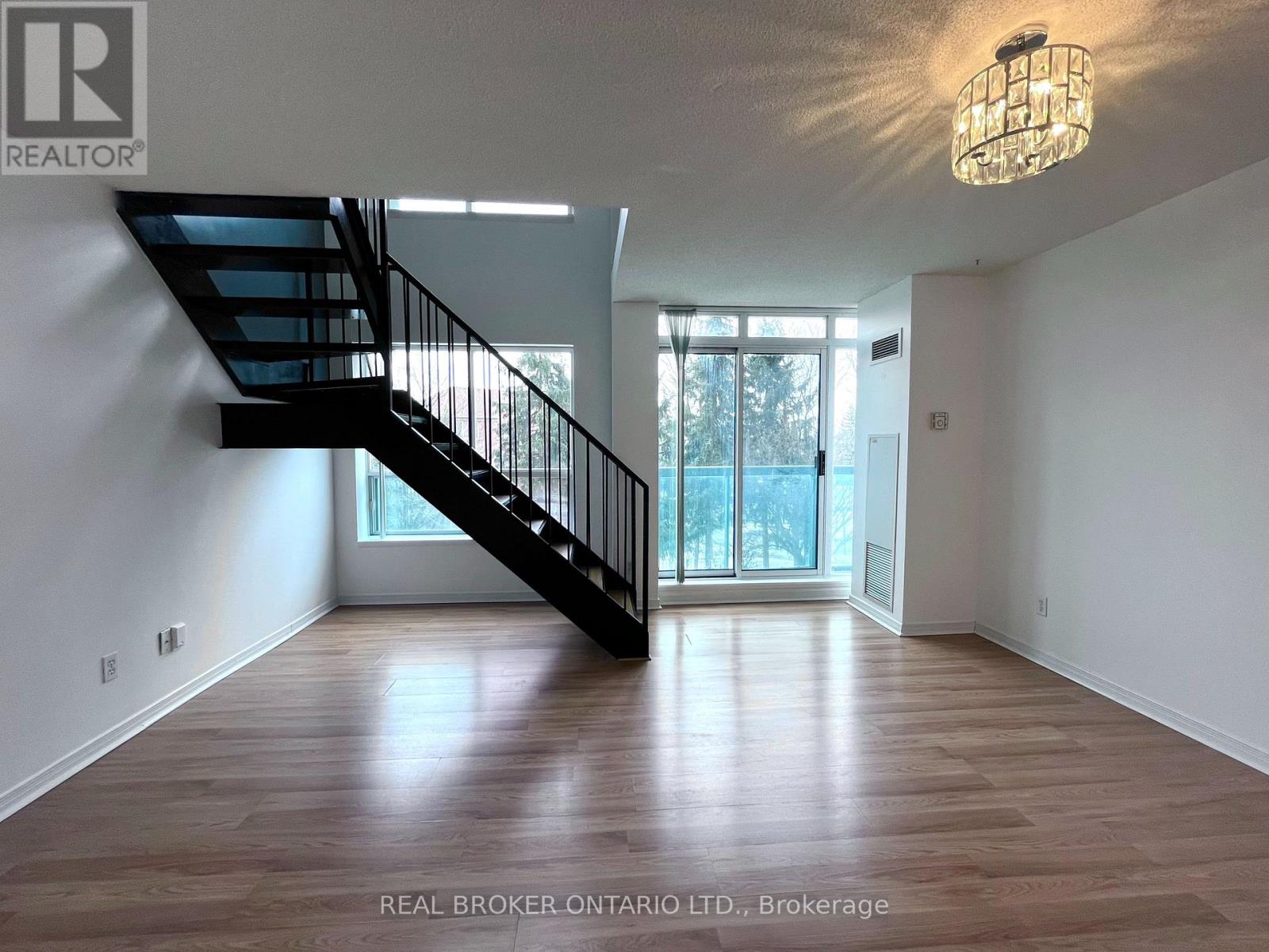 A spacious room with a wooden floor and a staircase leading to the upper level.