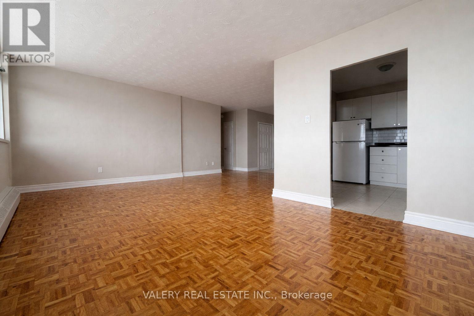 A room with wooden flooring and a kitchen area in the background.