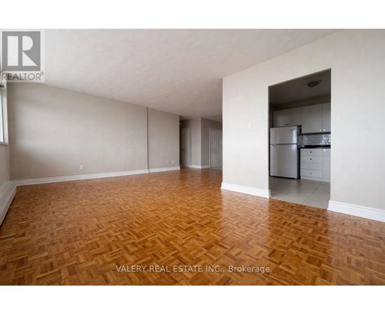 A room with wooden flooring and a kitchen area in the background.