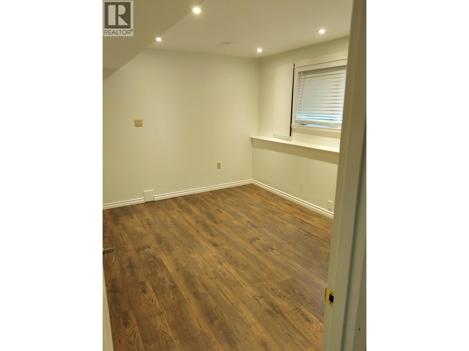 A room with wooden flooring and a window with blinds.