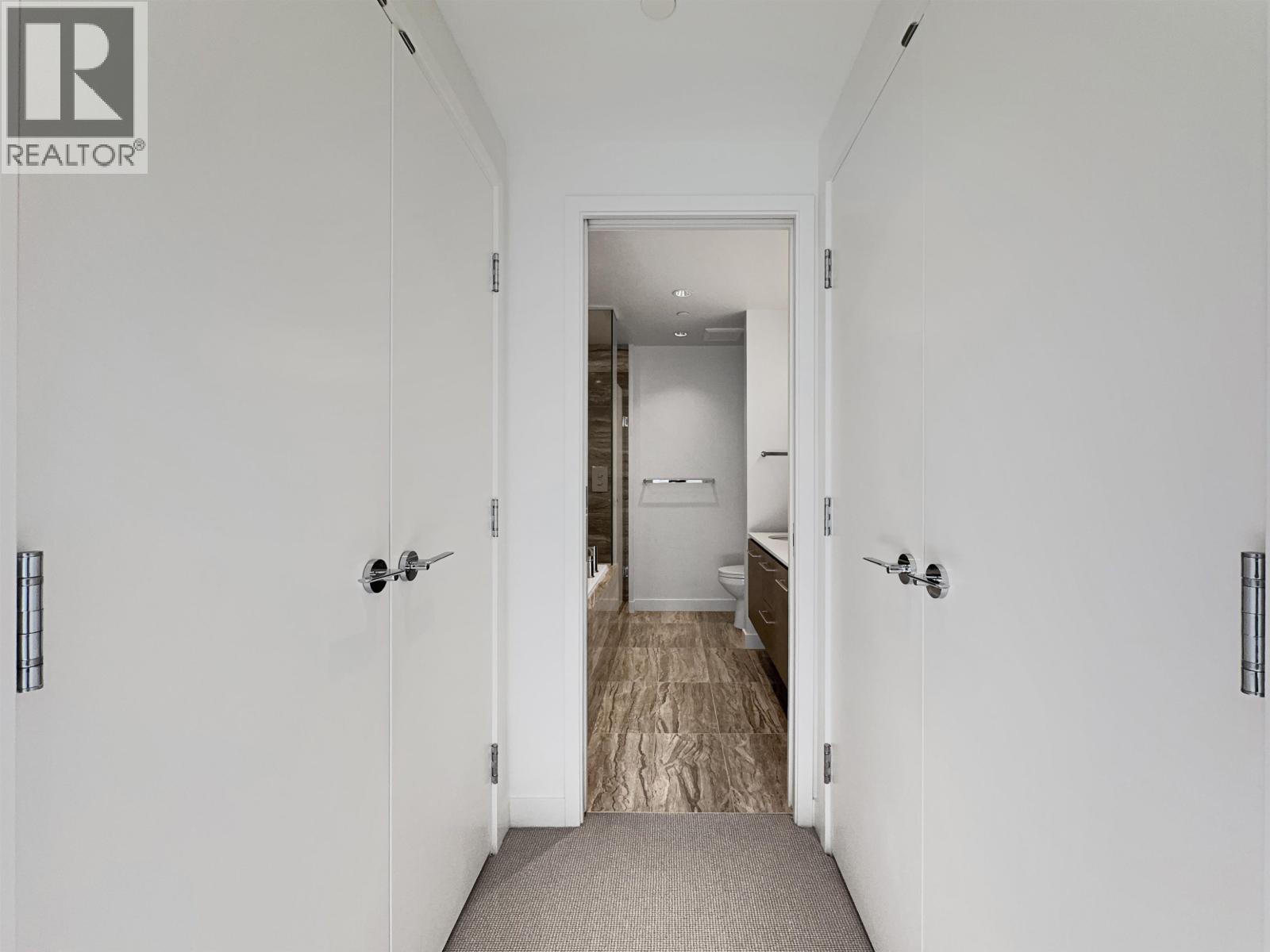 A hallway with a carpeted floor and white walls leading to a bedroom.