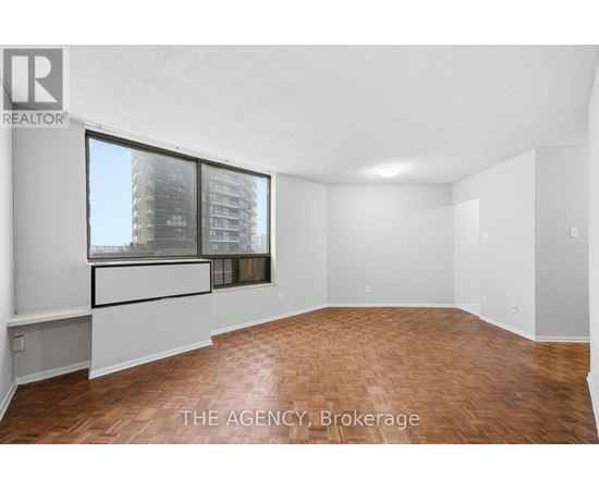 A spacious room with wooden flooring and a large window overlooking a cityscape.