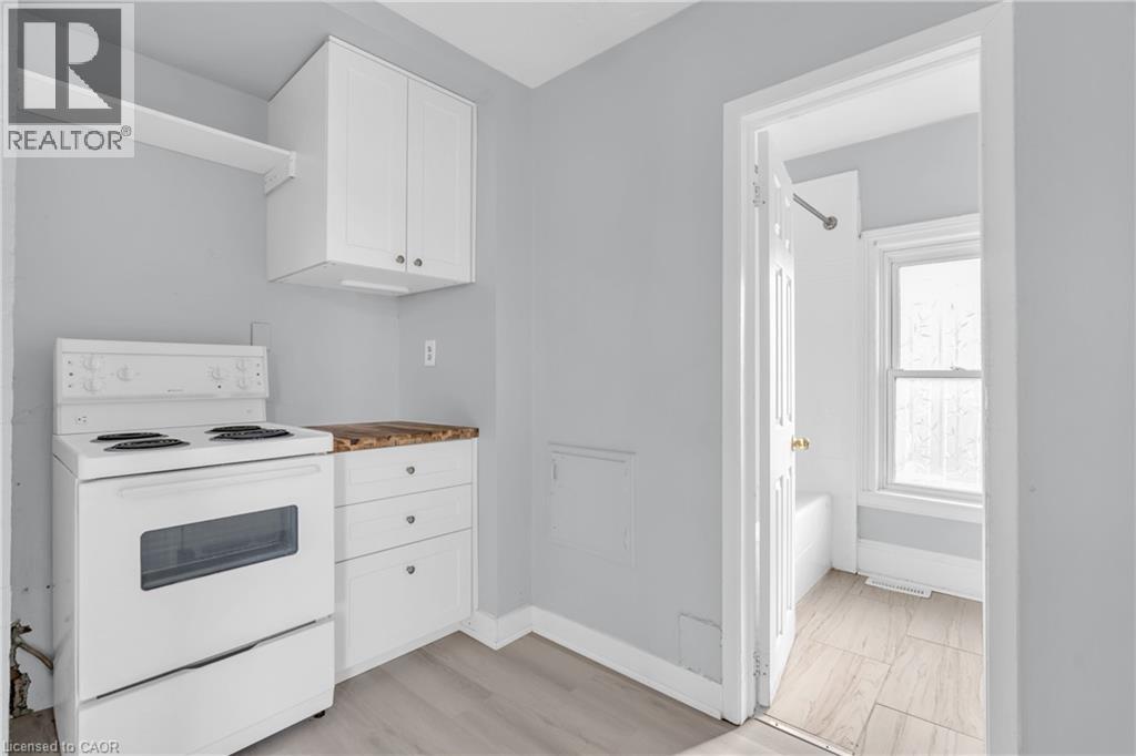 A white kitchen with a stove, cabinets, and a doorway leading to another room.