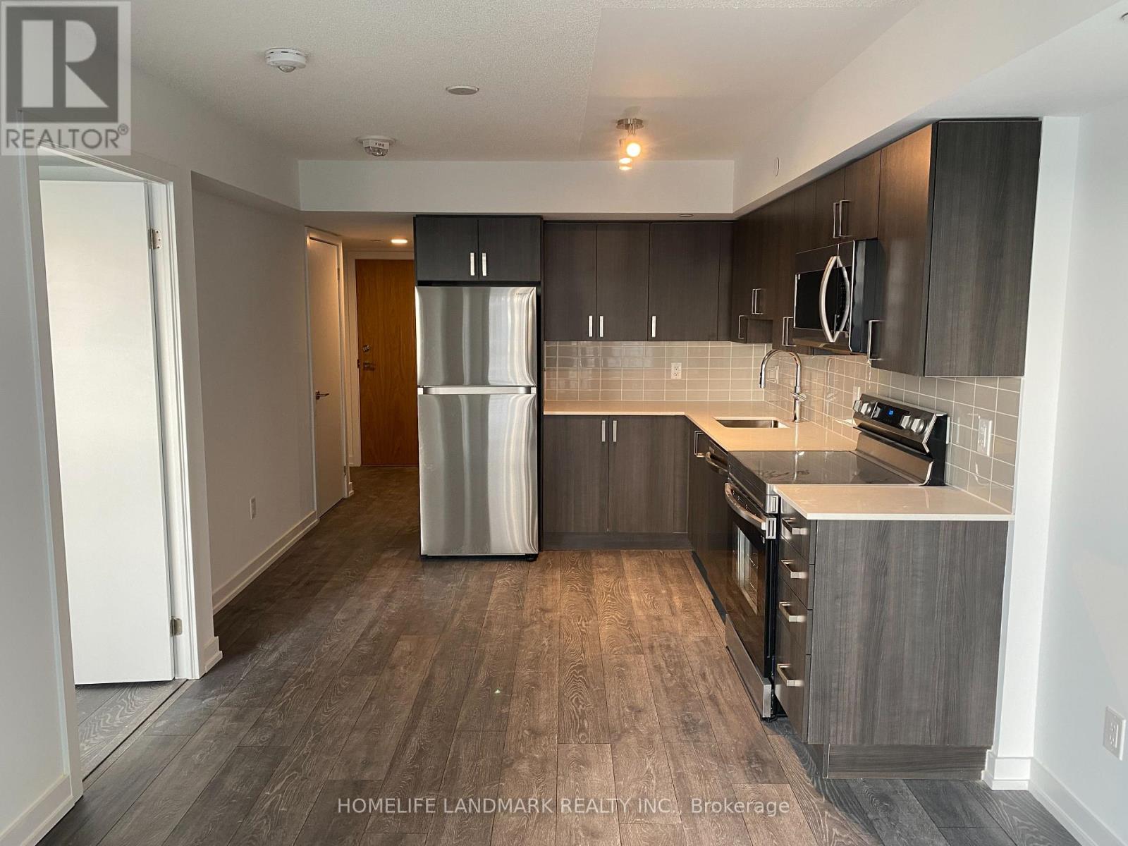 A modern kitchen with dark wood floors and stainless steel appliances.