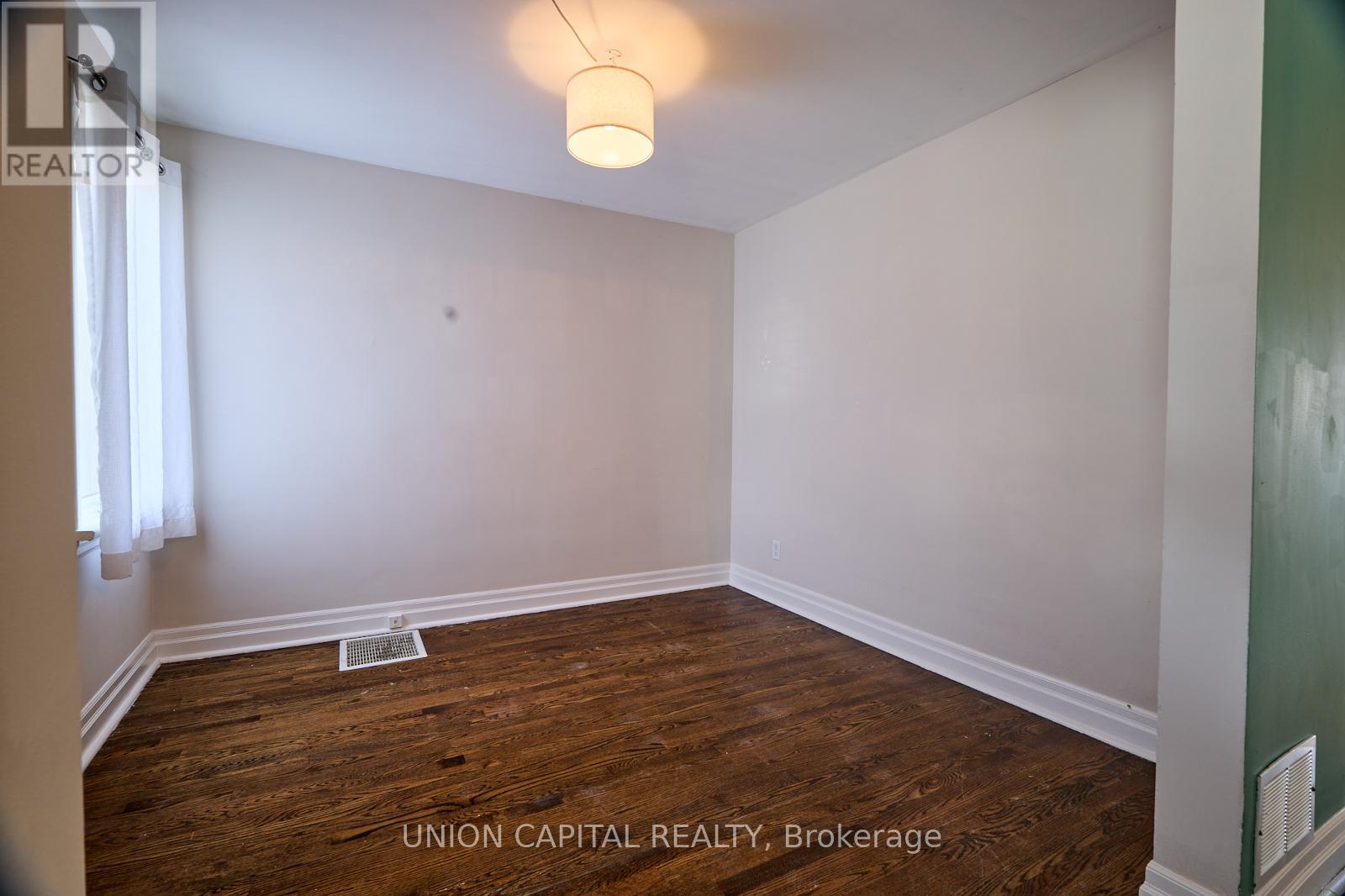 A room with wood flooring and white walls, with a light fixture hanging from the ceiling.