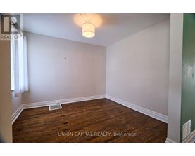A room with wood flooring and white walls, with a light fixture hanging from the ceiling.