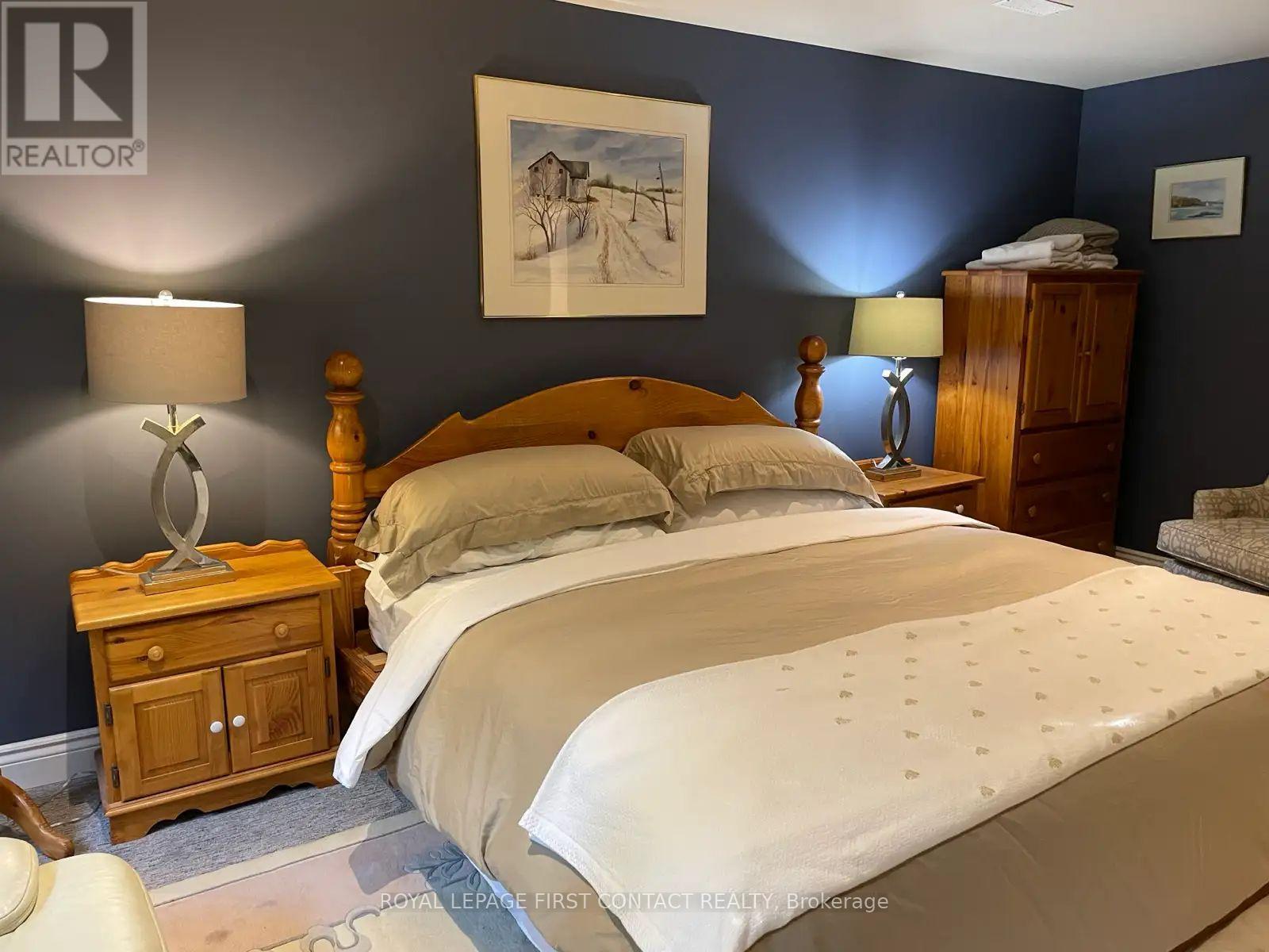 A bedroom with a large bed, a wooden nightstand, and a painting on the wall.