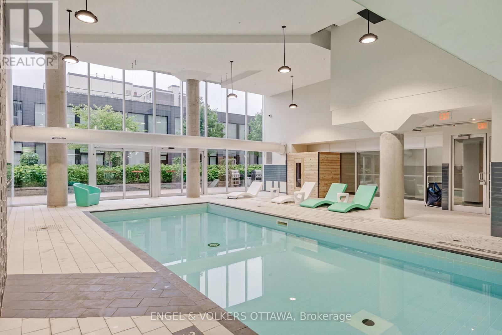 A large indoor swimming pool with a tiled floor and a sunny day outside.