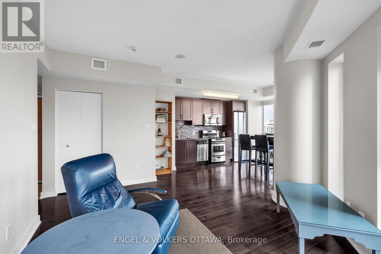 A blue chair sits in a living room with a kitchen in the background.