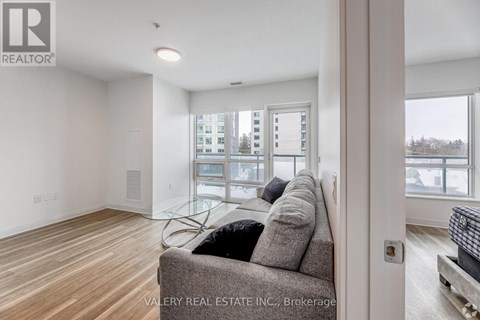 A living room with a grey couch and a window overlooking a parking lot.