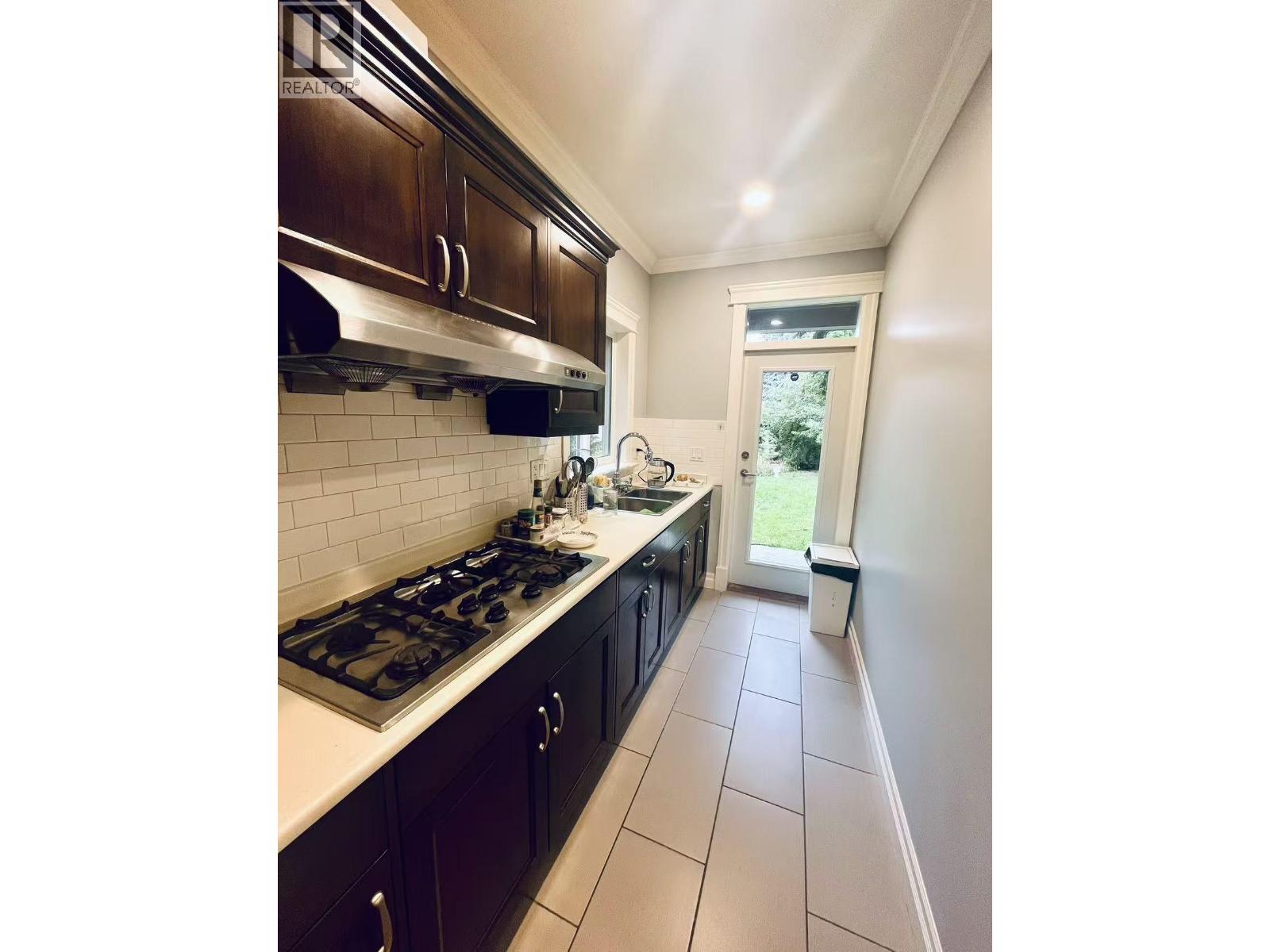A kitchen with a stove top oven and dark brown cabinets.