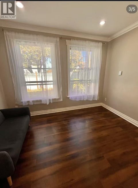 A living room with a black couch and a window with white curtains.
