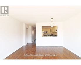 A realtor photo of an empty room with a picture of a kitchen in the background.