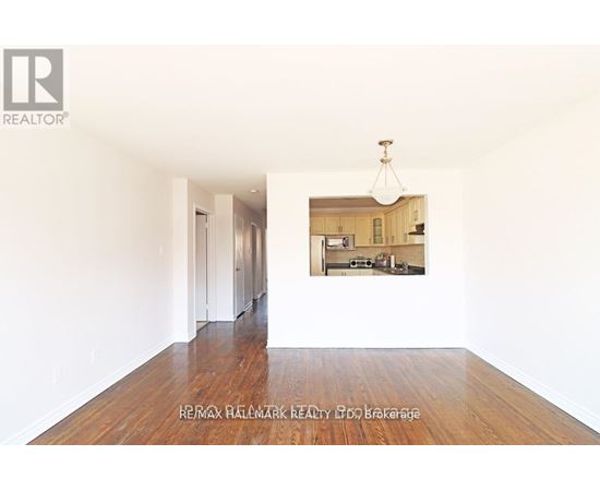 A realtor photo of an empty room with a picture of a kitchen in the background.