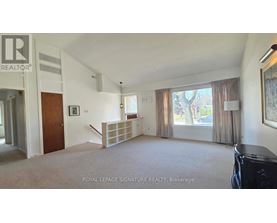 A spacious living room with a carpeted floor and a large window with curtains.