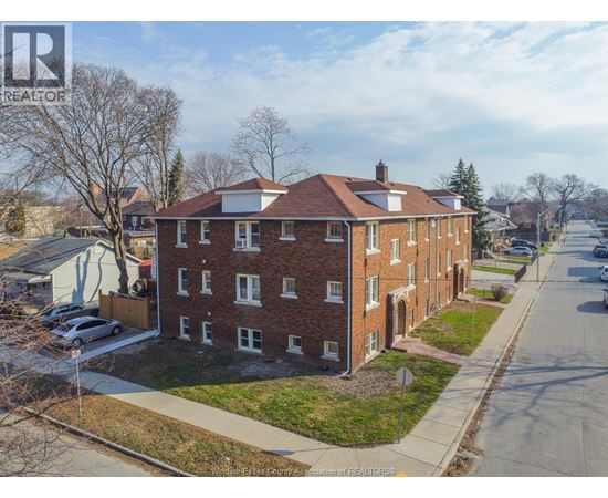 A brick apartment building with a white roof and a car parked in front.