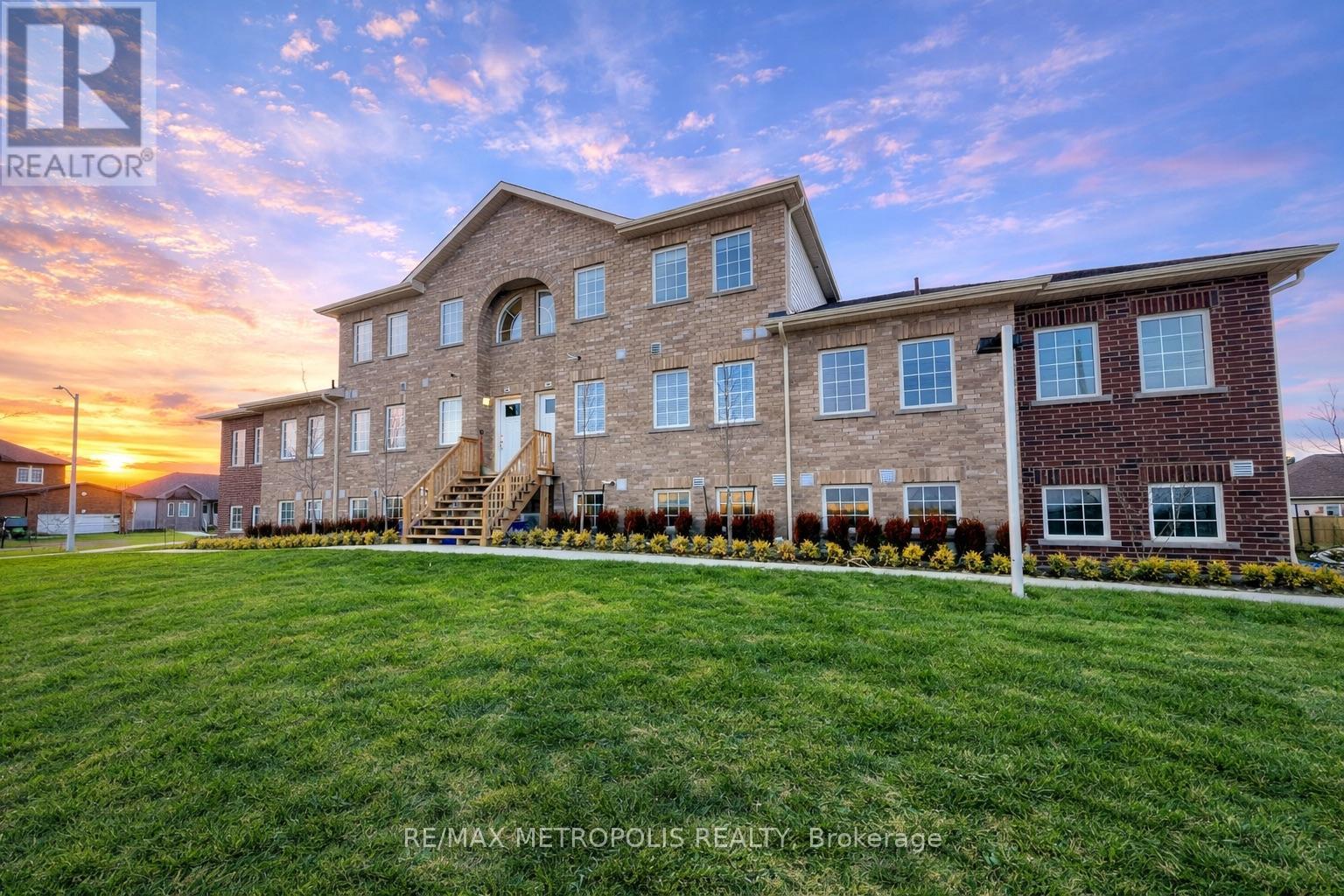A large brick building with a grassy front yard and a sunset in the background.
