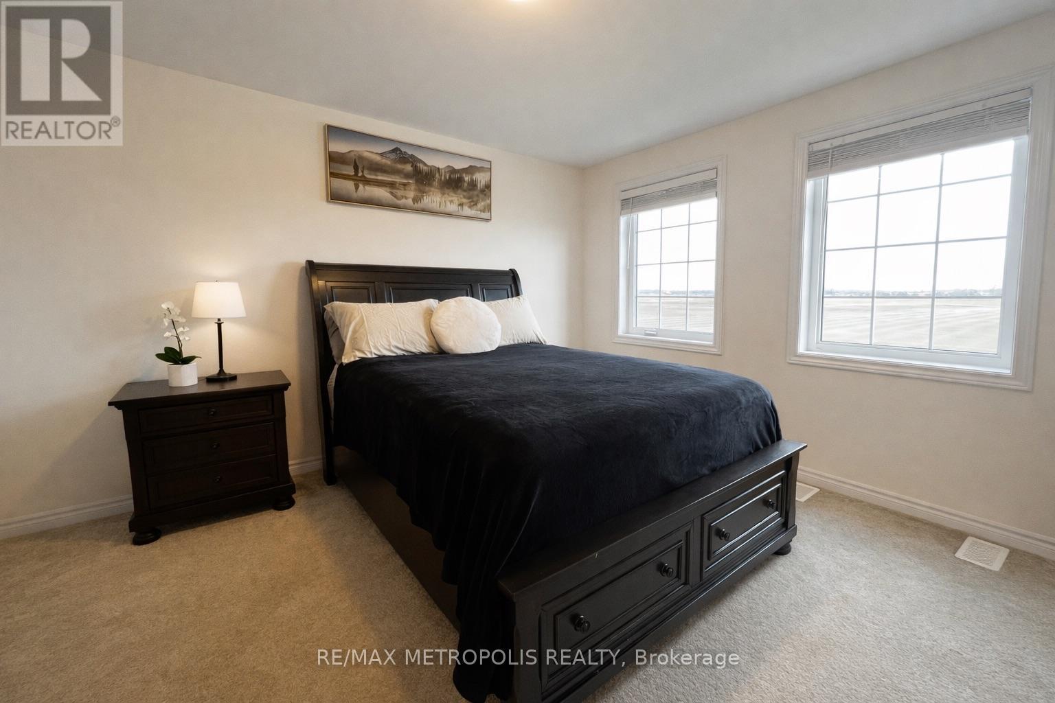 A bedroom with a large bed, a nightstand with a lamp, and a painting on the wall.