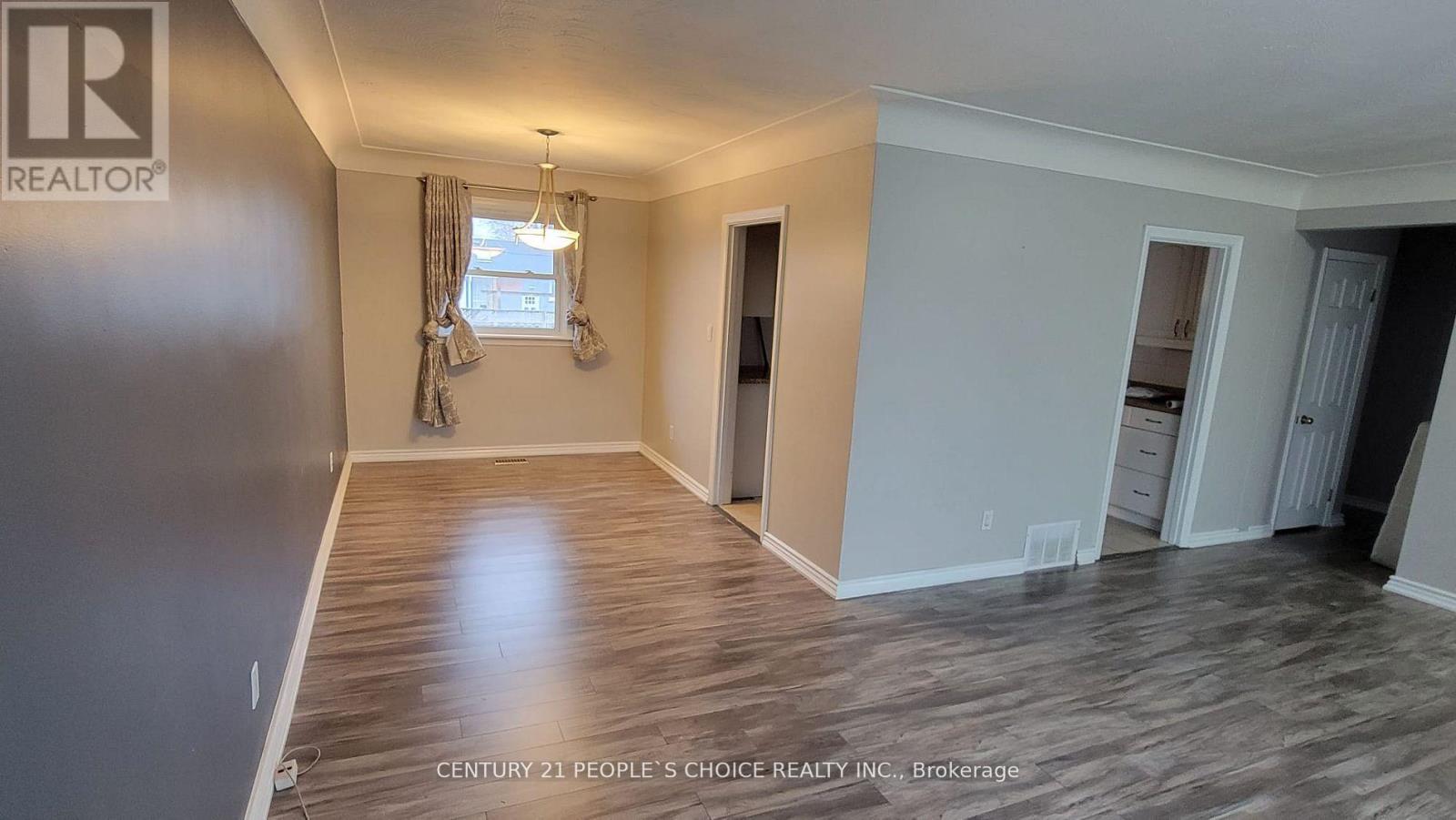 A spacious room with wooden flooring and a window with curtains.