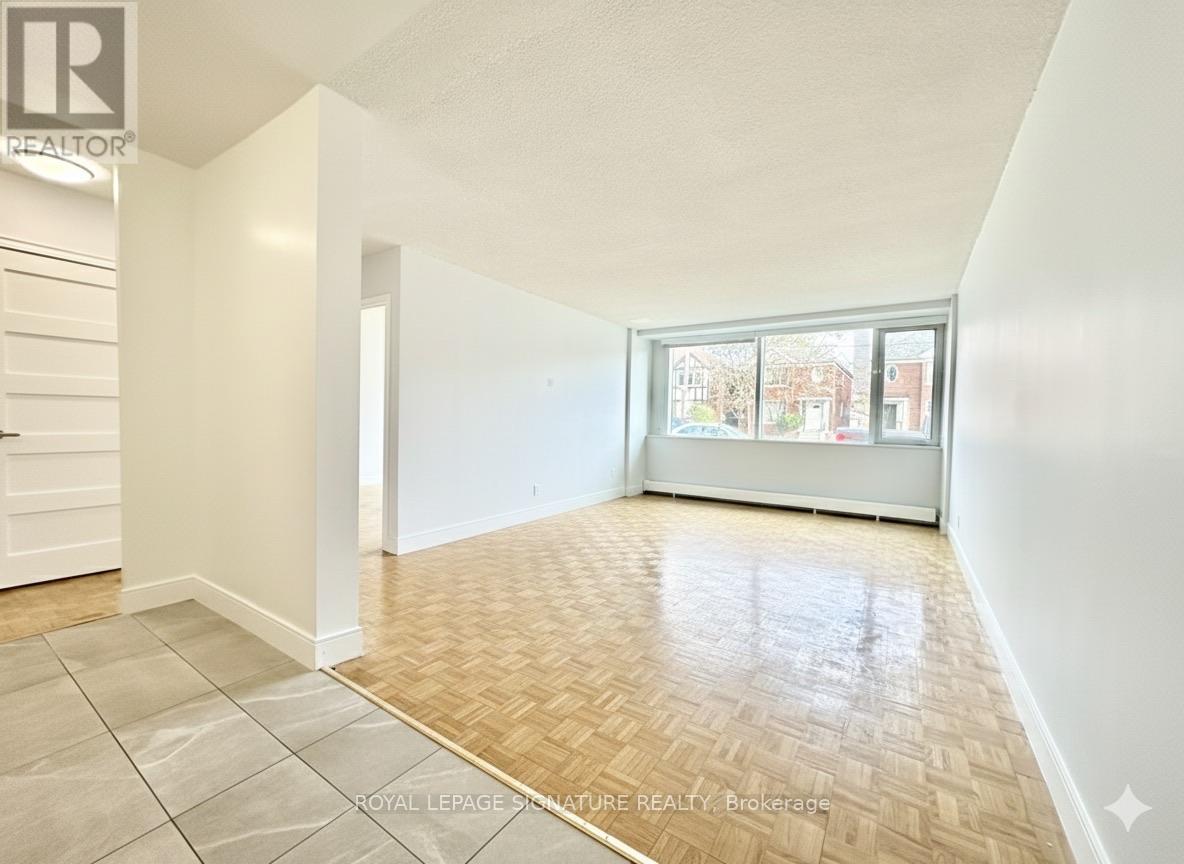 A room with a wooden floor and a large window showing a view of buildings outside.