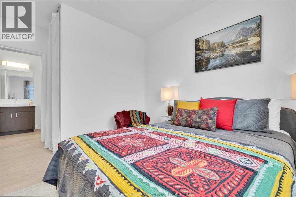 A bedroom with a bed covered in a multicolored quilt and a painting hanging on the wall.