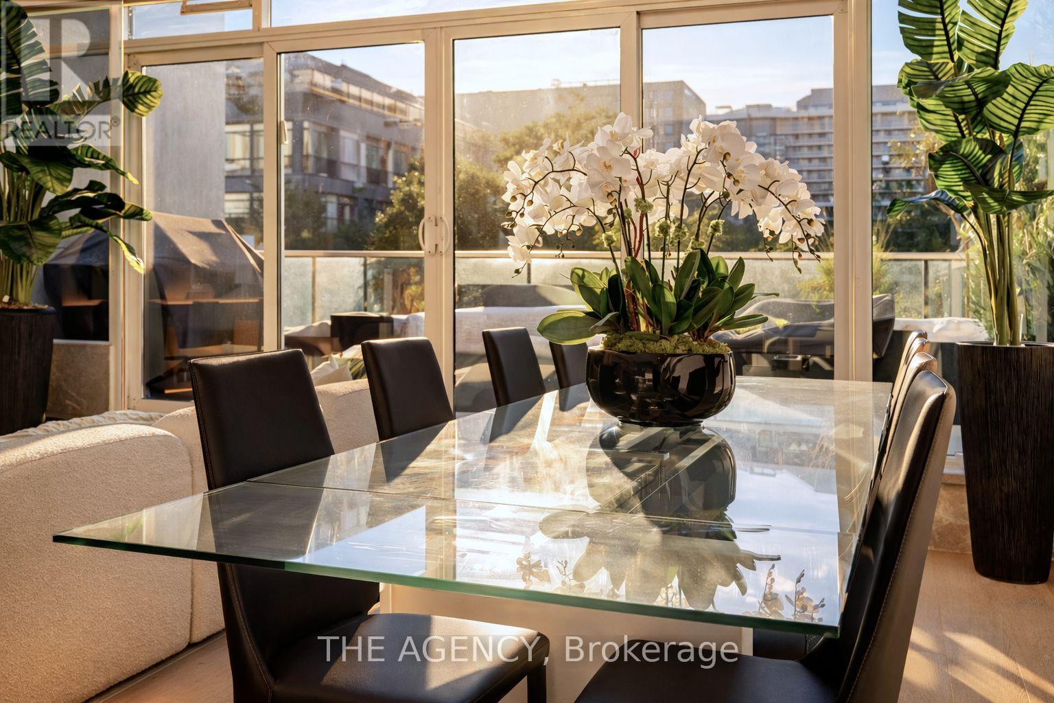 A glass table with chairs and a vase of flowers in the middle of it.