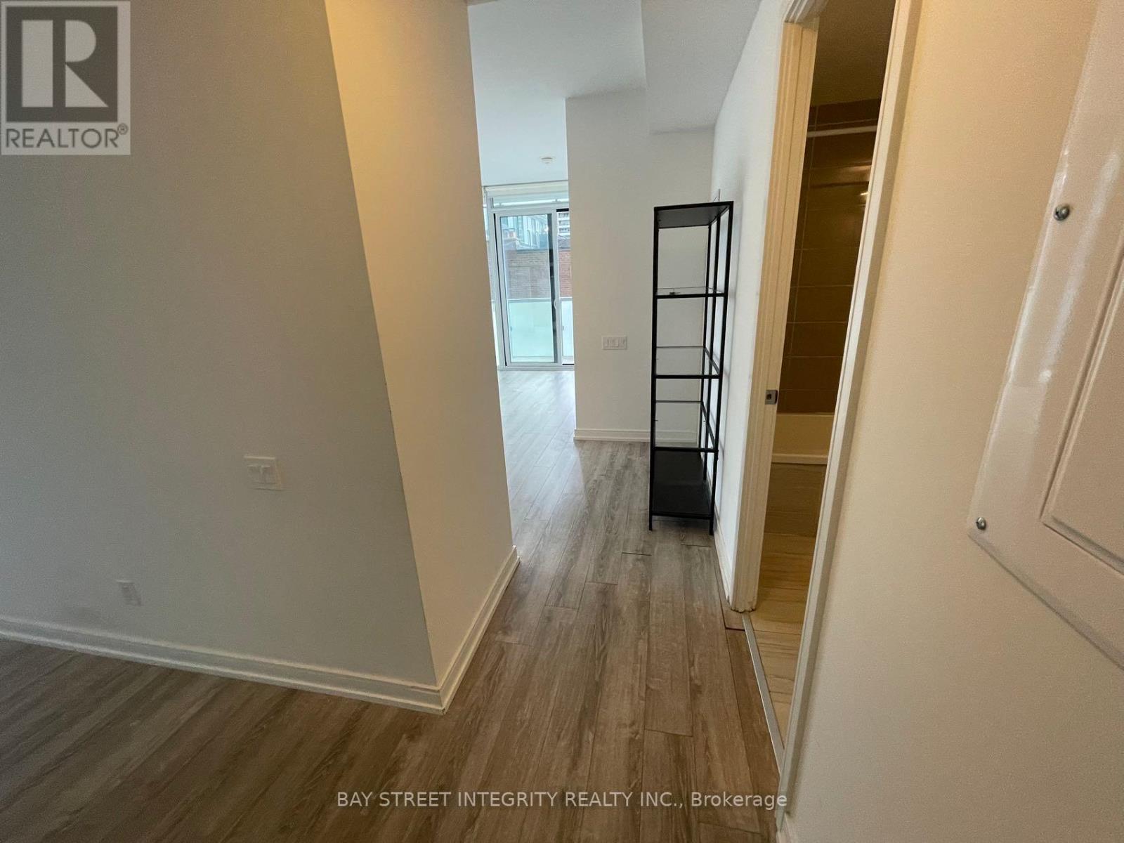 A hallway with wood flooring and white walls, leading to a door with a black frame.