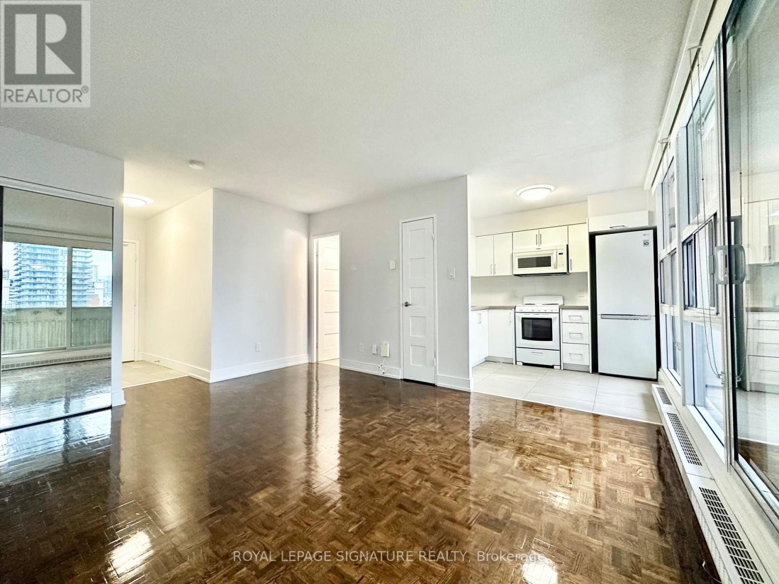 A spacious room with wooden flooring and a kitchen area with white appliances.