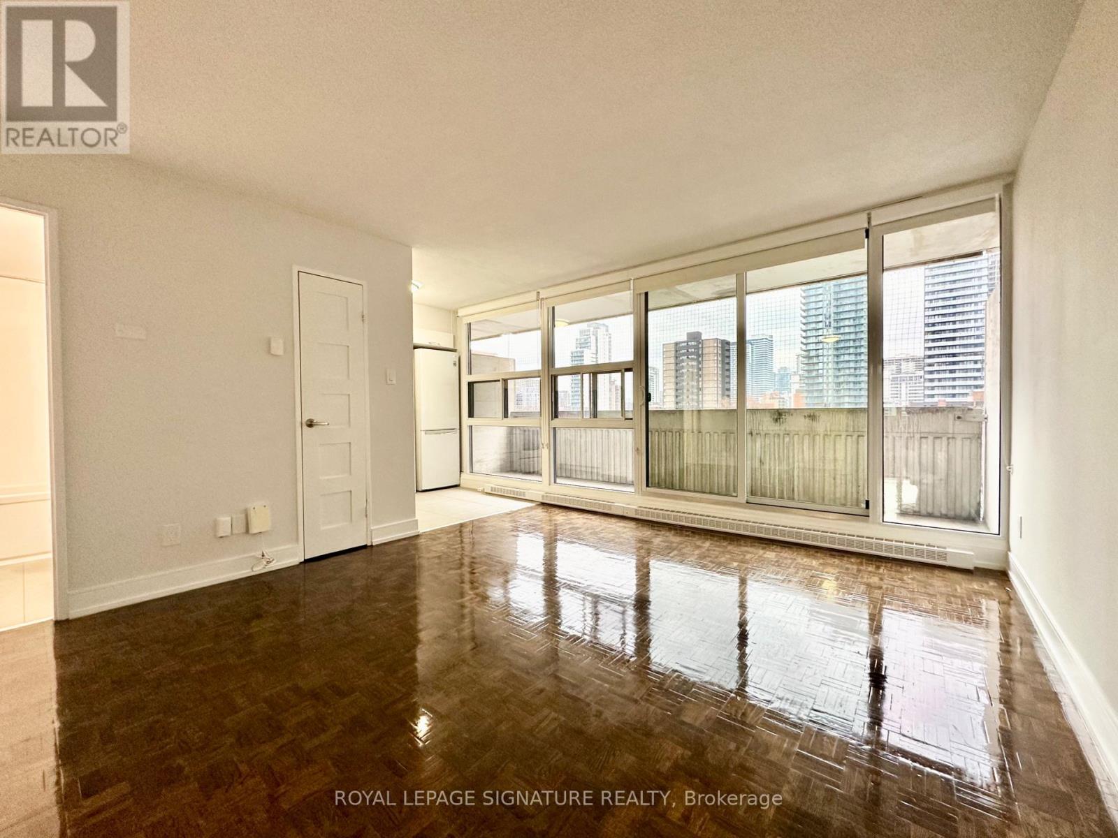 A spacious room with wooden flooring and large windows overlooking a cityscape.
