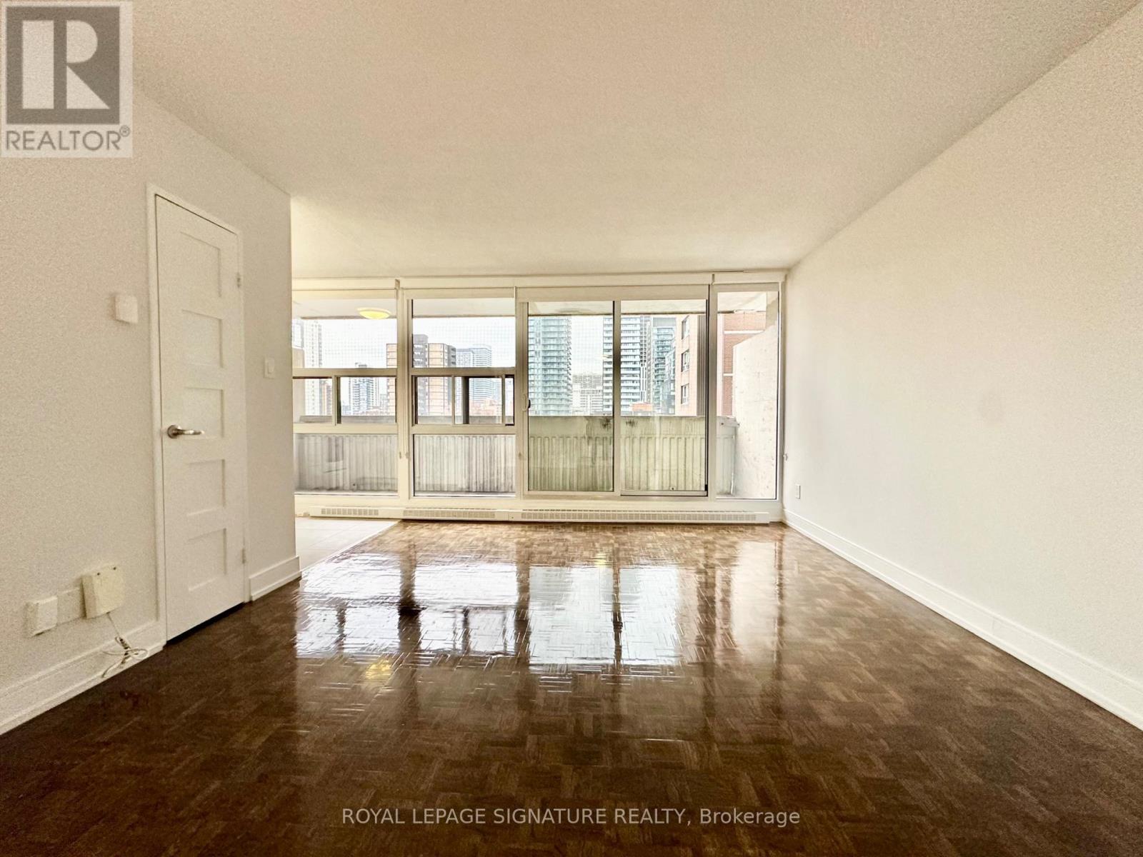 A room with a wooden floor and a large window with a view of buildings outside.
