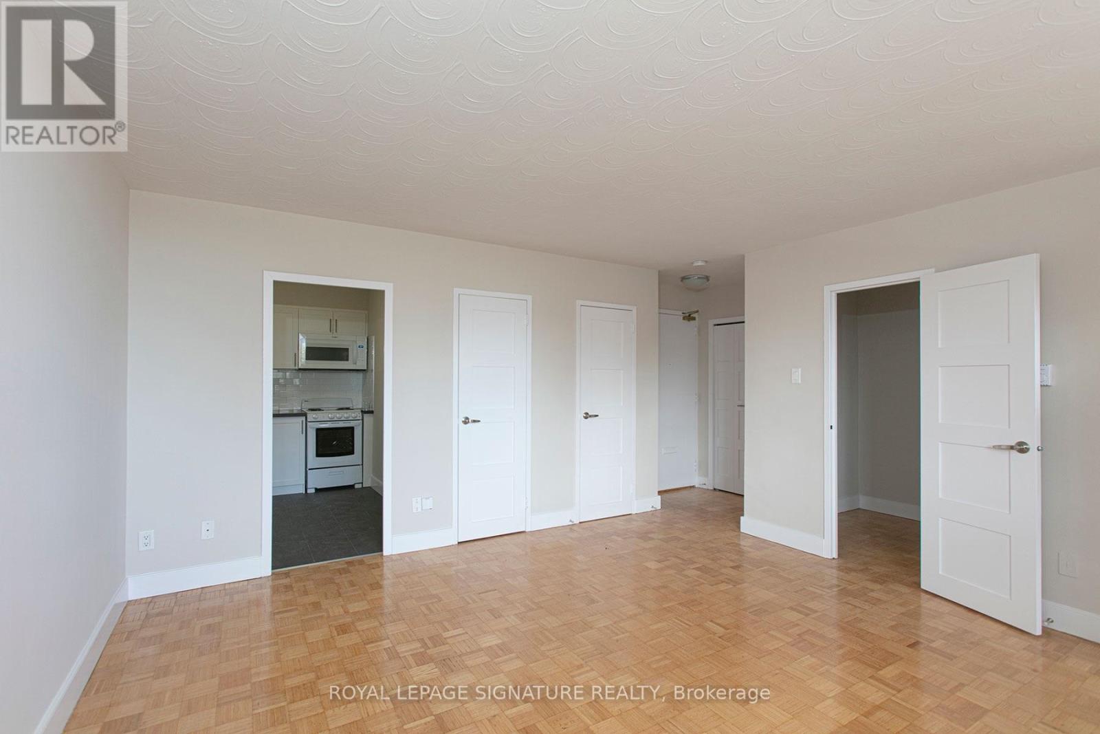 A white room with a kitchen in the background and a doorway leading to another room.